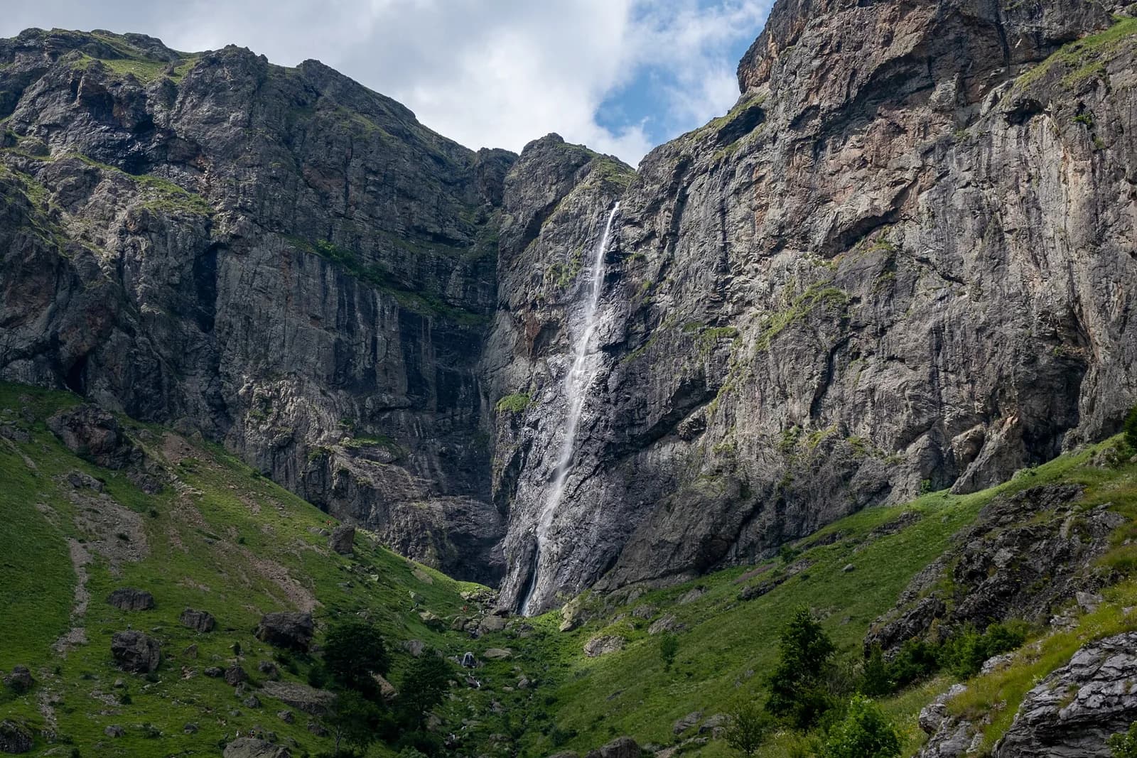 Raysko Praskalo waterfall falling down a tall cliff above green slopes