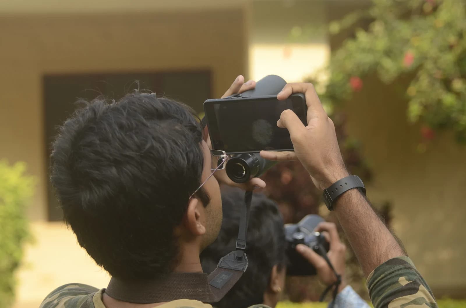 A birdwatcher holds a smartphone against binoculars to take a photograph.
