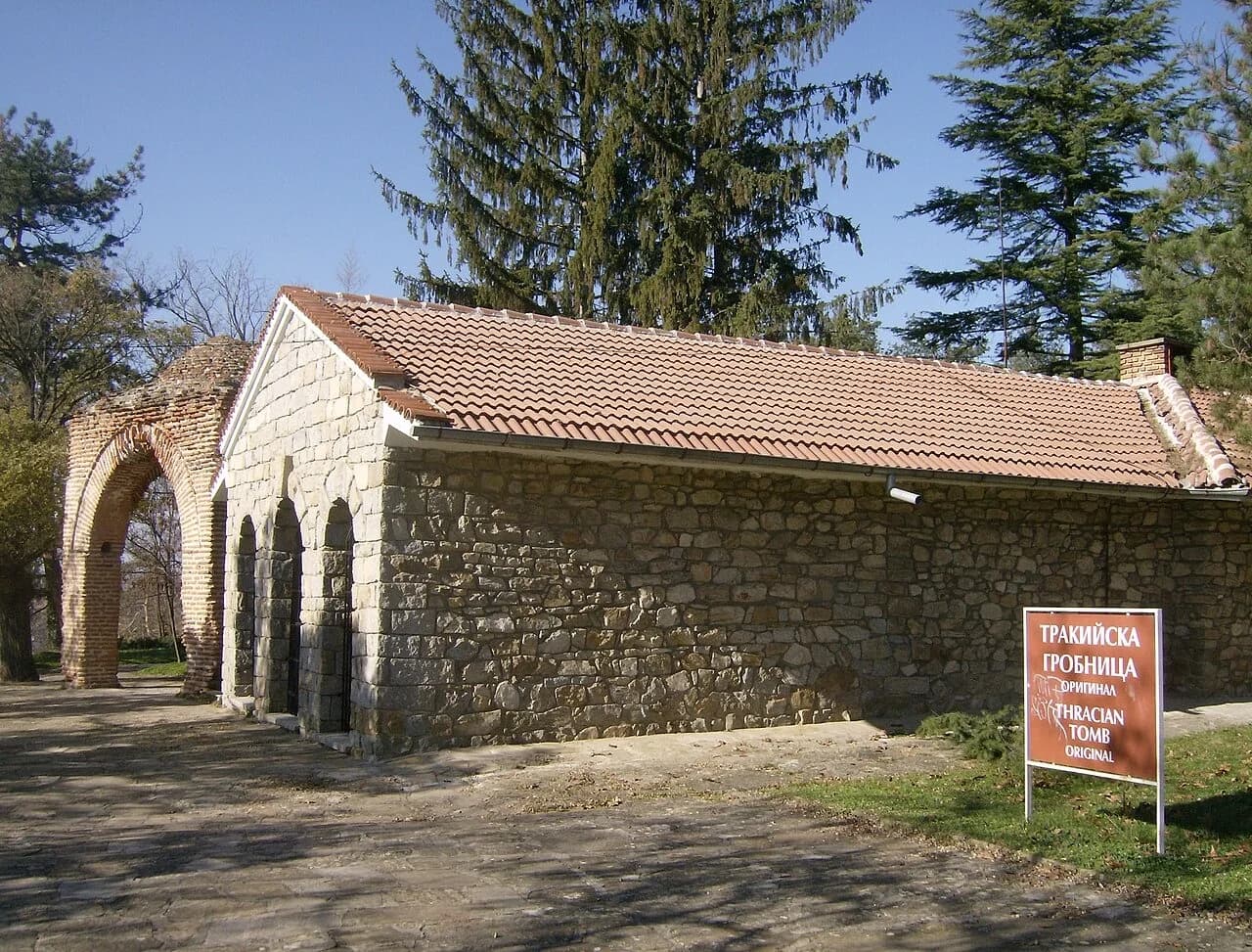 Stone building with a tiled roof and a brick arch, beside a sign reading Thracian Tomb Original, in Kazanlak