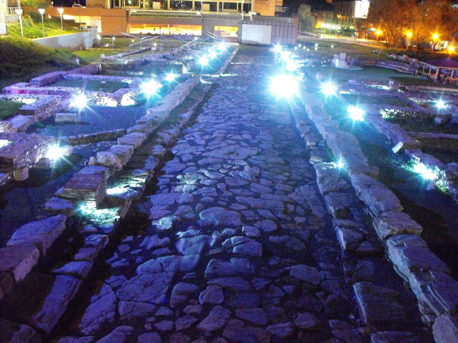 An illuminated Roman stone road at the Augusta Traiana forum after dark.