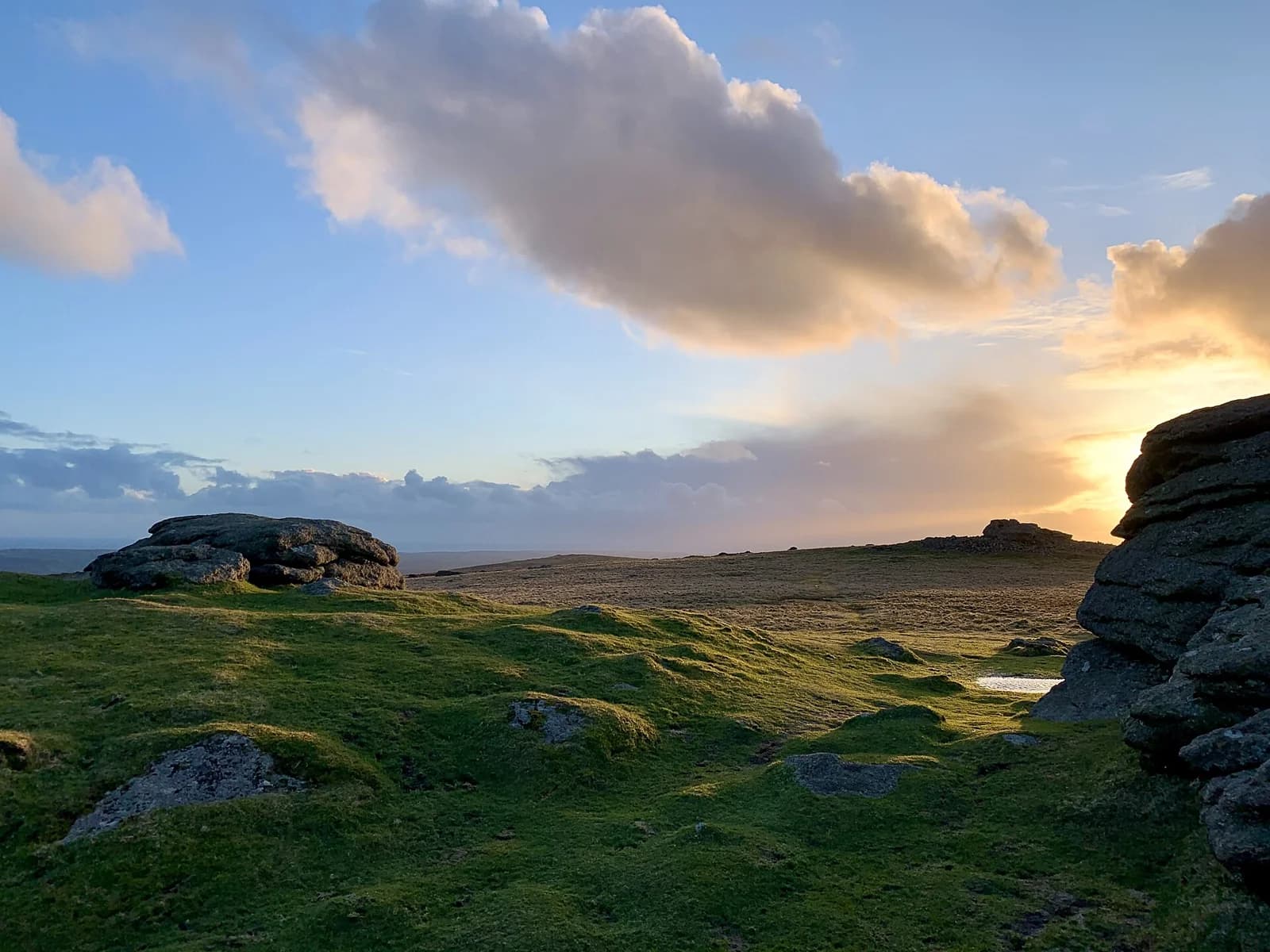Rocky grassland in Dartmoor beneath clouds lit by the setting sun.