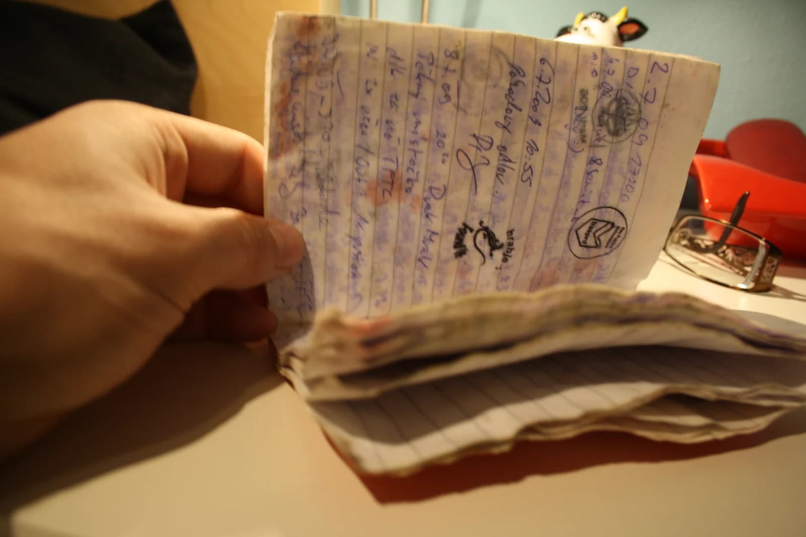 A hand holds open a geocache logbook covered in handwritten entries.