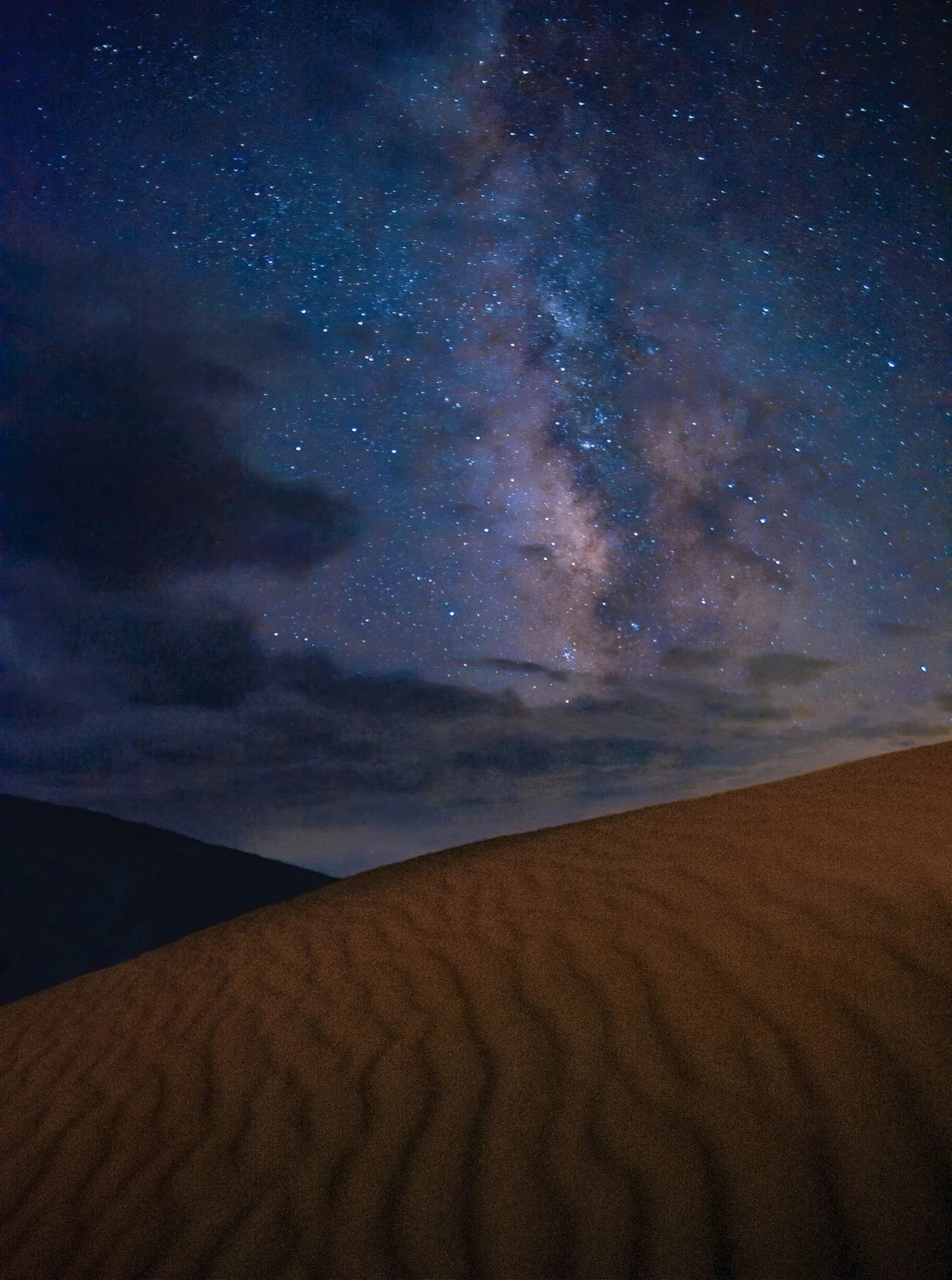 The Milky Way and clouds above a rippled sand dune at Great Sand Dunes.