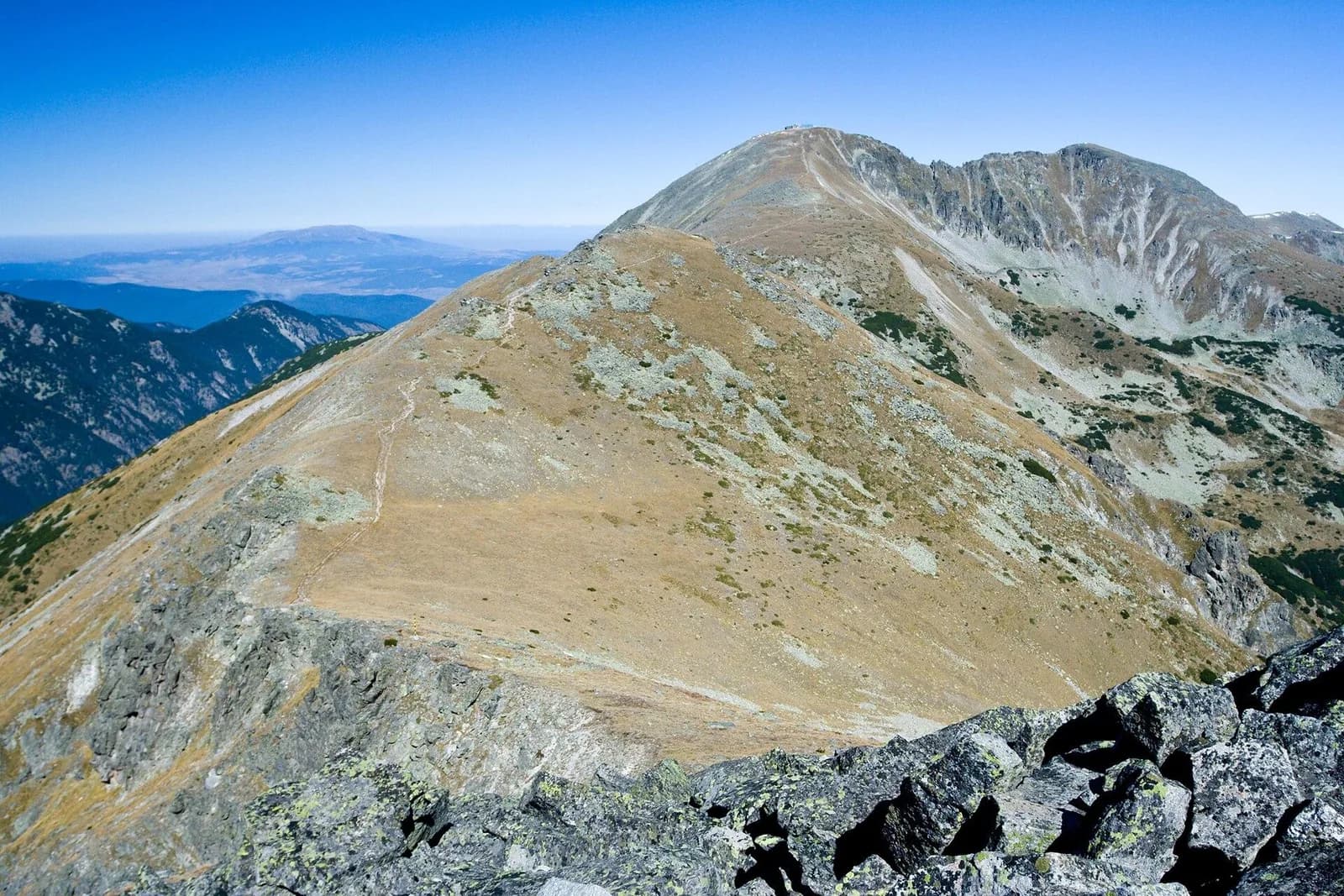 Musala’s rocky summit ridge rises above bare mountain slopes under a blue sky.