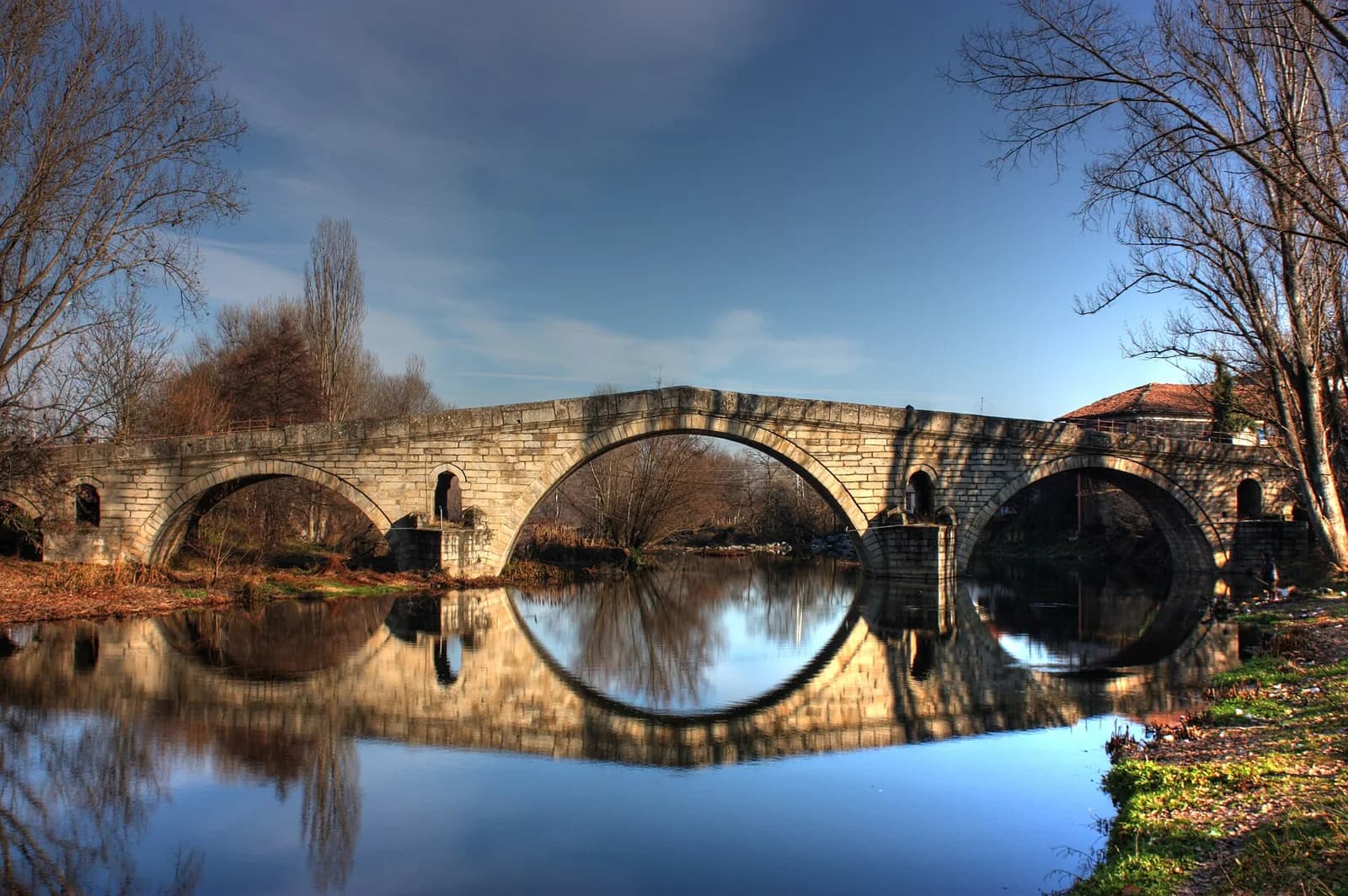 Stone arches of Kadin Bridge reflected in the river at Nevestino