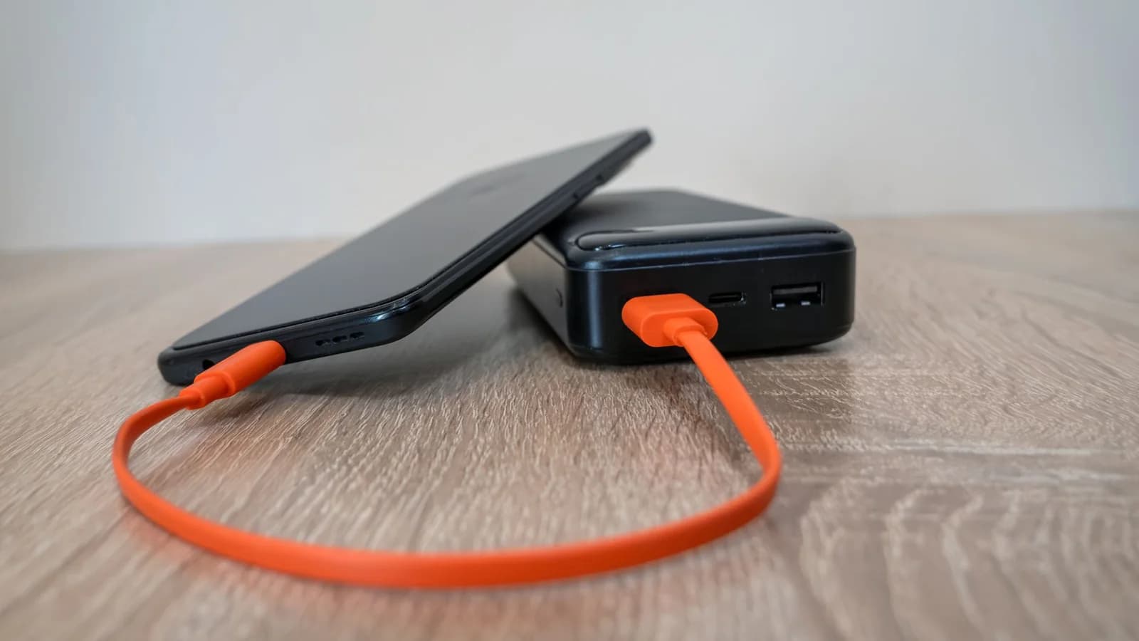 A smartphone connected to a black power bank by an orange USB cable