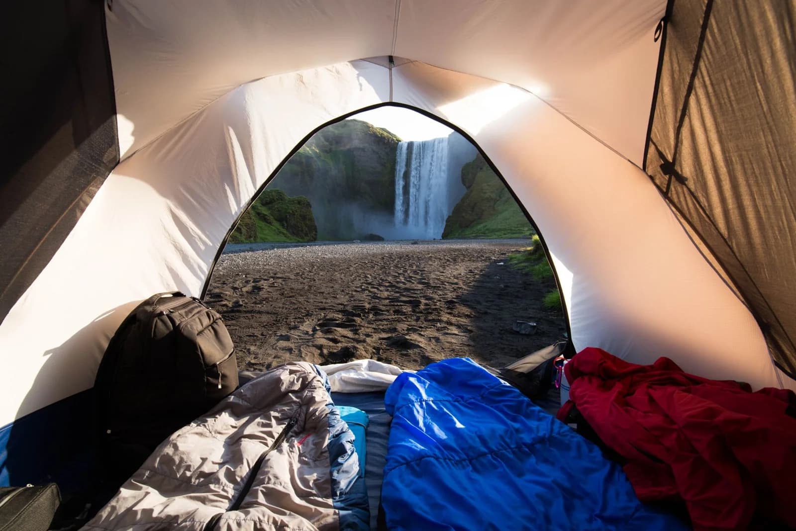 Sleeping bags and a backpack inside a tent overlooking a waterfall
